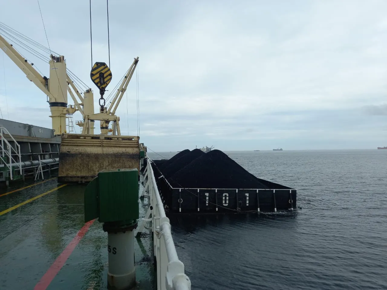 Tongkang bermuatan batu bara di samping kapal dengan crane dan grab